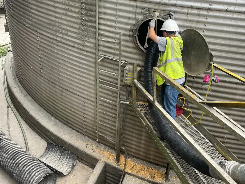 Worker entering grain bin with vacuum hose for silo cleaning